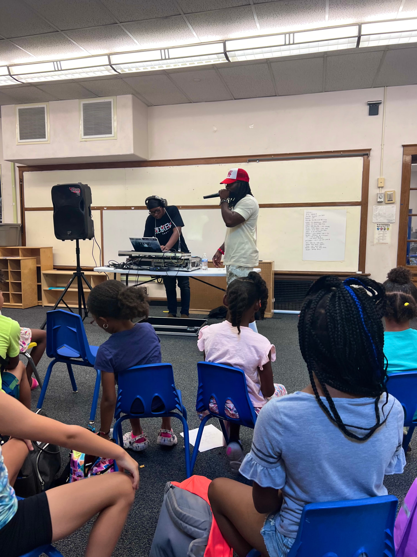 Young people seated together as a facilitator and DJ lead a music session